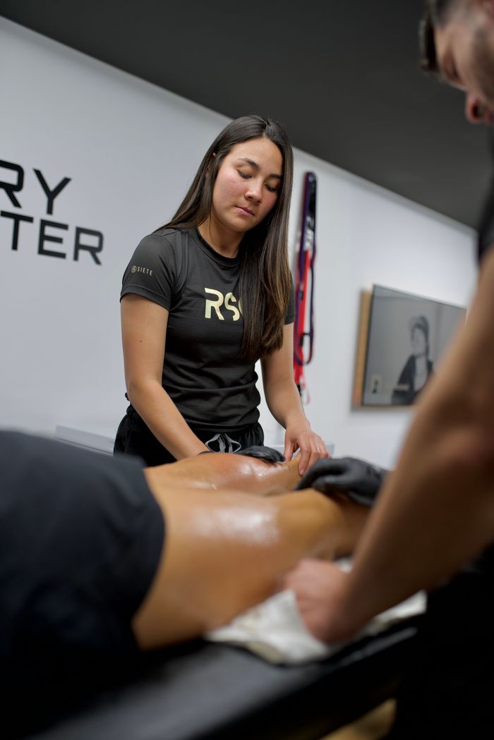 A sports therapist provides a massage session in a recovery center, focusing on muscle therapy.